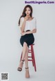 A woman sitting on a red stool wearing a white top and black skirt.