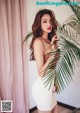 A woman in a white dress posing next to a palm tree.