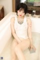 A woman sitting in a bathtub with a tattoo on her arm.