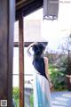 A woman in a blue and white dress standing in front of a window.